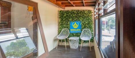 Un balcón de madera con puerta de vidrio, dos sillas blancas y una pared verde con un letrero.
