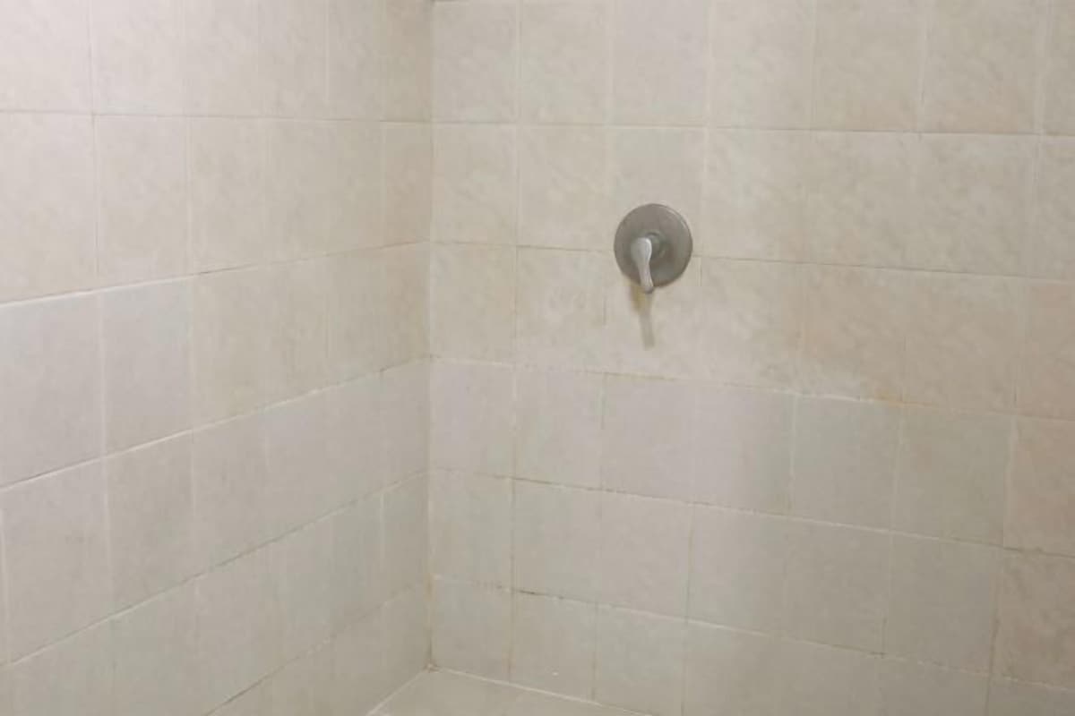 A corner of a room with tiled walls and a shower control panel.