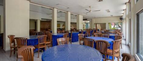A large indoor dining area with round tables covered with blue tablecloths and wooden chairs.