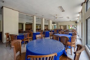 A large indoor dining area with round tables covered with blue tablecloths and wooden chairs. - Mahajaya Hotel Denpasar (Bali)