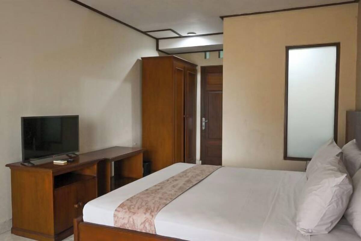 A bedroom with a bed, a TV on a wooden stand, and a wardrobe.