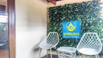 Eine Wand mit einem grünen, belaubten Hintergrund und einem Schild für 'MAHAJAYA Hotel & Convention'. Zwei weiße Stühle mit Gewebedesign sind vorhanden.