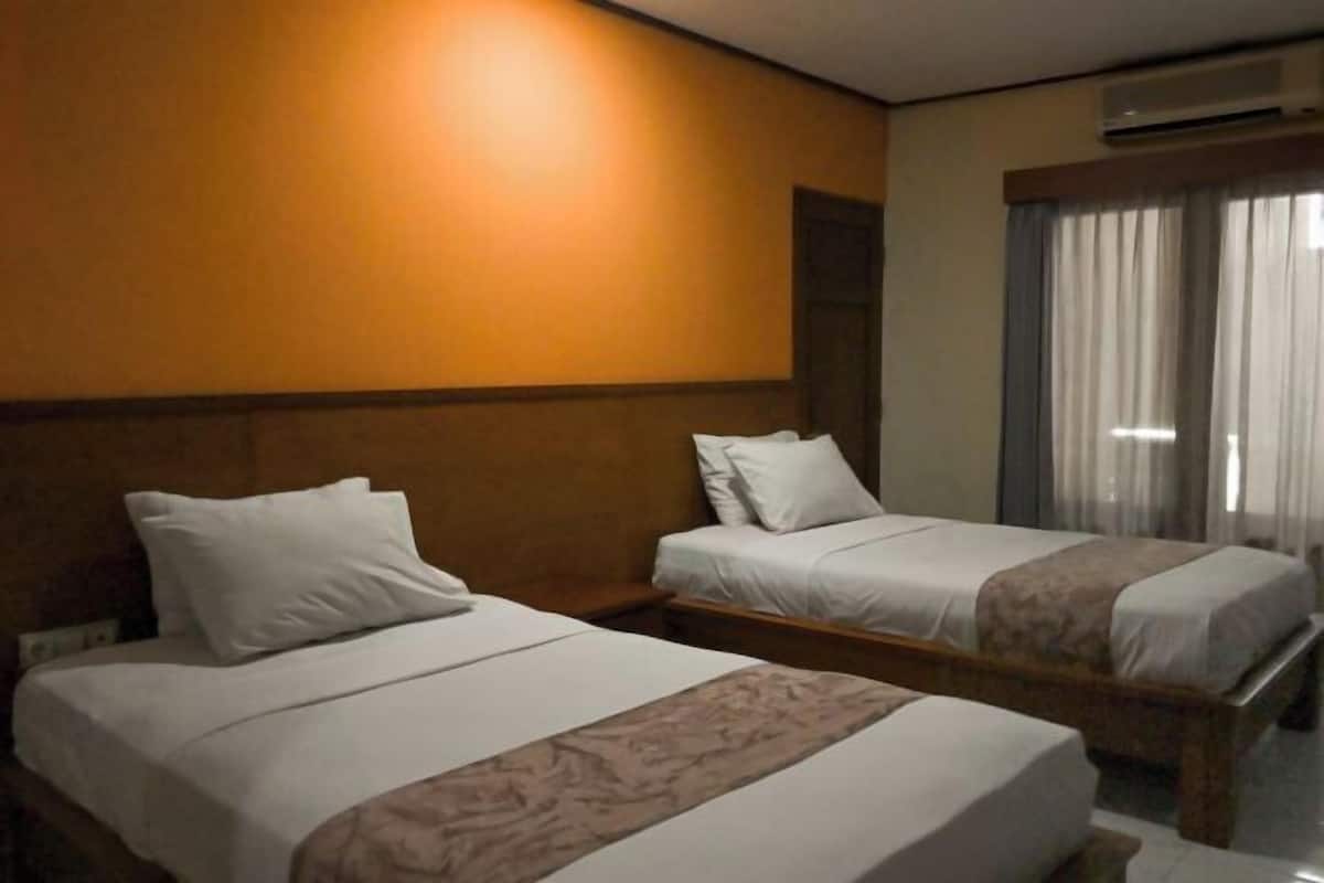A hotel room with two single beds, a wooden headboard, a large mirror, and a window with curtains.