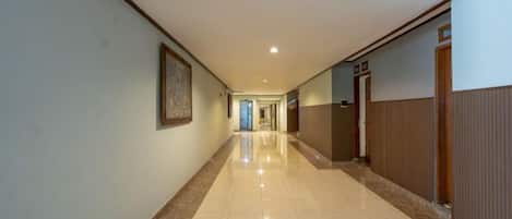 A long, narrow hallway with a tiled floor, a framed picture on the left wall, and a door on the right.