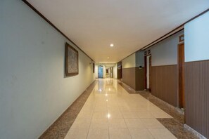 A long, narrow hallway with a tiled floor, a framed picture on the left wall, and a door on the right. - Mahajaya Hotel Denpasar (Bali)