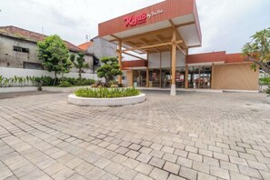 A commercial building with a covered entrance and a landscaped area with plants. - Mahajaya Hotel Denpasar (Bali)