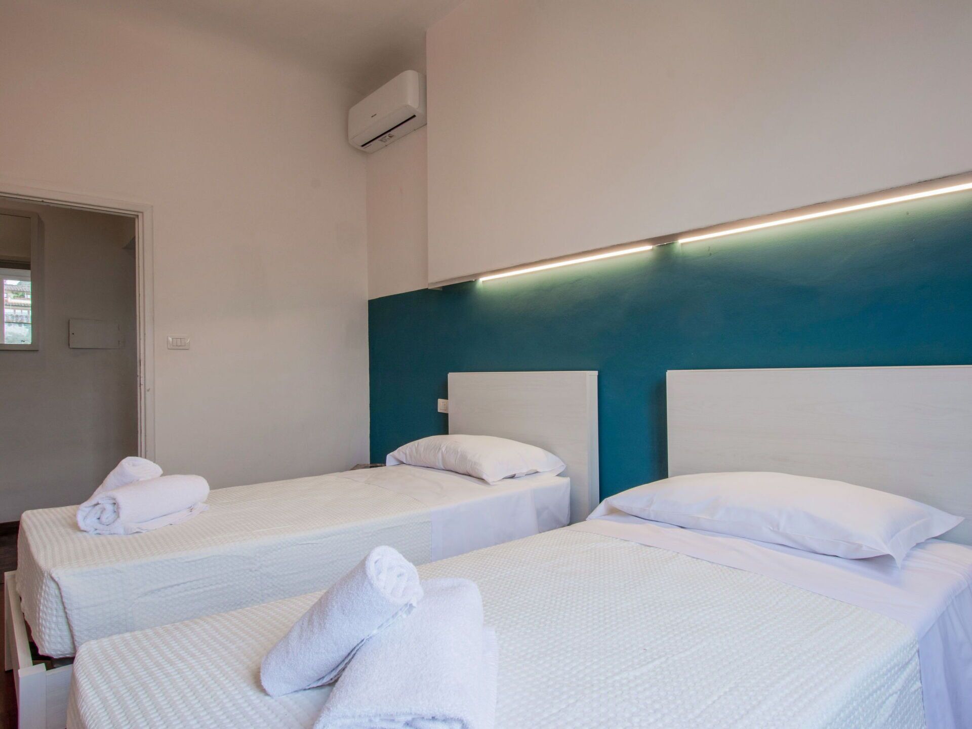 A hotel room with two single beds, each with a white headboard and pillows, and a small bedside table.
