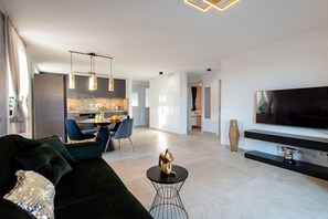 Een moderne woonkamer met een donkergroene bank, een zwarte salontafel en een flatscreen televisie aan de wand.