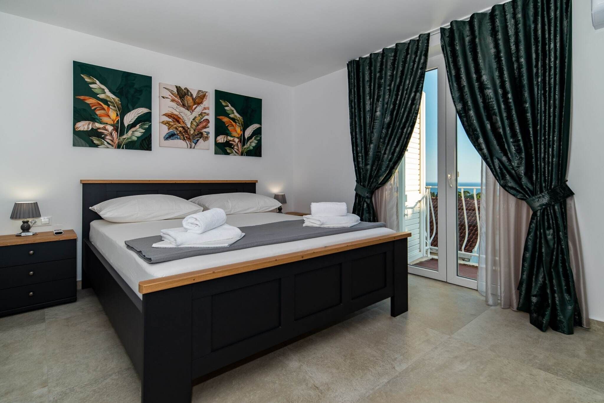 A bedroom with a bed, a nightstand, a lamp, and a view of the outside.