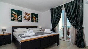 A bedroom with a bed, a nightstand, a lamp, and a view of the outside.