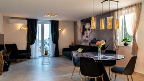A modern dining area with a round table, black chairs, and pendant lights. There is a sofa and a small side table with a vase of flowers.