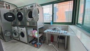Een wasserette met meerdere wasmachines, een droogrek en een klein tafeltje met een geruit tafelkleed.