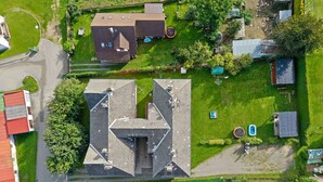 Vista aerea di una zona residenziale con una casa di grandi dimensioni e dalla forma particolare, una piscina e un cortile recintato.