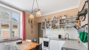 Una cucina con un tavolo di legno, sedie, un fornello e mensole piene di oggetti da cucina.