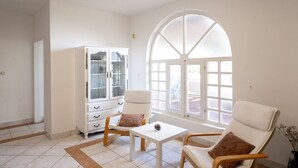 Une pièce comprenant deux fauteuils blancs, une petite table blanche et un meuble blanc doté de portes en verre.