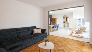 Un salon moderne avec un canapé foncé, une table basse blanche et un parquet en bois disposé en motif chevrons.