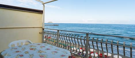A balcony with a table and chairs, overlooking a beach with umbrellas and a pier.