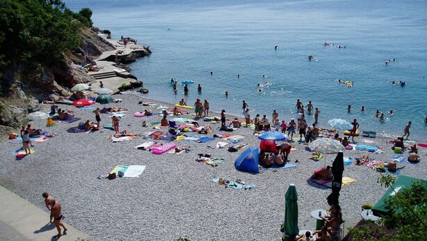 Ein voller Strand mit Menschen, die sich sonnen und schwimmen.