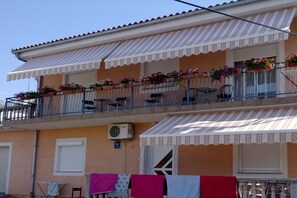 Un edificio de dos pisos con un balcón decorado con plantas en macetas y un toldo blanco.