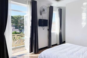 Een hotelkamer met een bed, een televisie, een plafondventilator en een balkon met gordijnen.