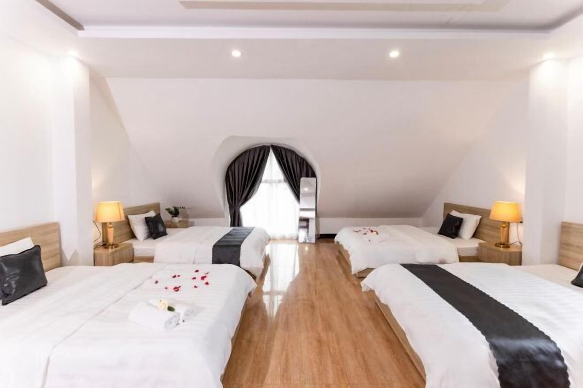 Une chambre d’hôtel avec deux lits, un plancher en bois et une grande fenêtre avec des rideaux.