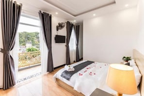A bedroom with a bed, a bedside lamp, a TV on the wall, and a balcony with curtains.