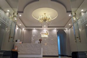 Een hotel receptie met een marmeren balie, een kroonluchter en een bordje met de tekst 'Hotel'.