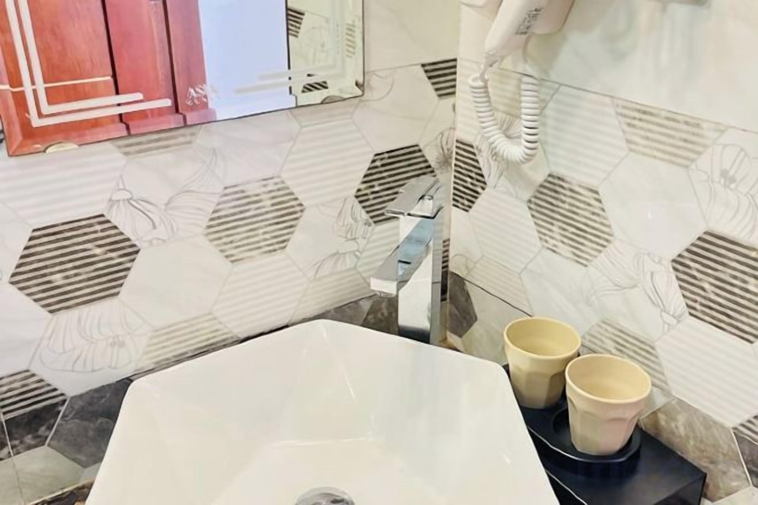 A bathroom with a white sink, two beige cups on a black tray, and a hexagonal patterned wall.