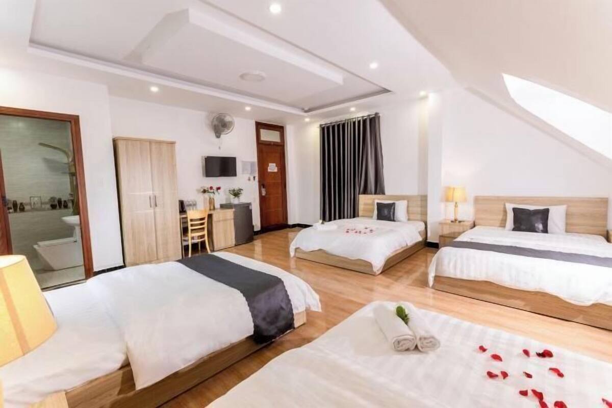 A hotel room with two beds, a desk, a chair, a TV, and a large window with curtains.