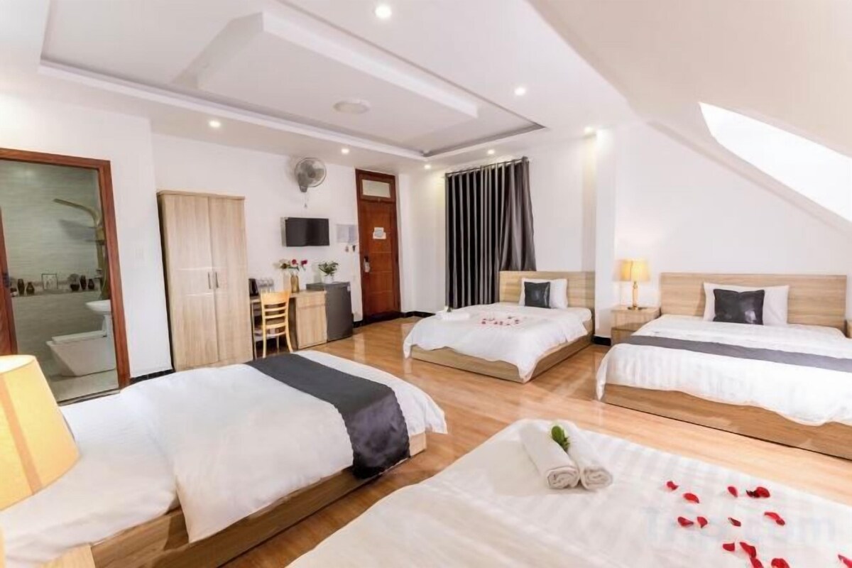 A hotel room with two beds, a desk, a chair, and a shower area.