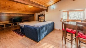 Ein gemütliches Zimmer mit Holzbalkendecke, einem Bett, einem Fernseher und einer Essecke mit Stühlen und Tisch.