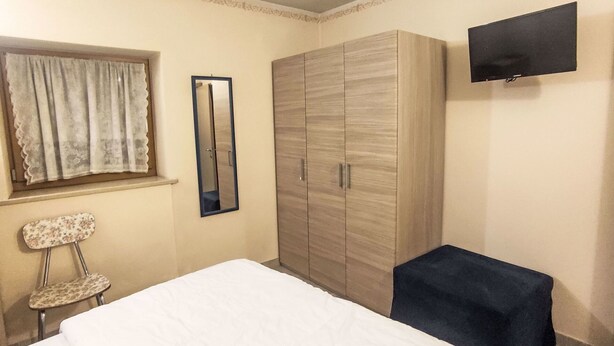Un dormitorio con cama, armario, silla, mesita, espejo y televisor.