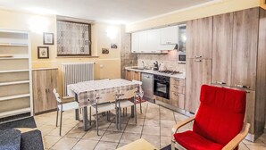 Una cocina compacta con armarios blancos, una mesa de comedor con sillas y un sillón rojo.
