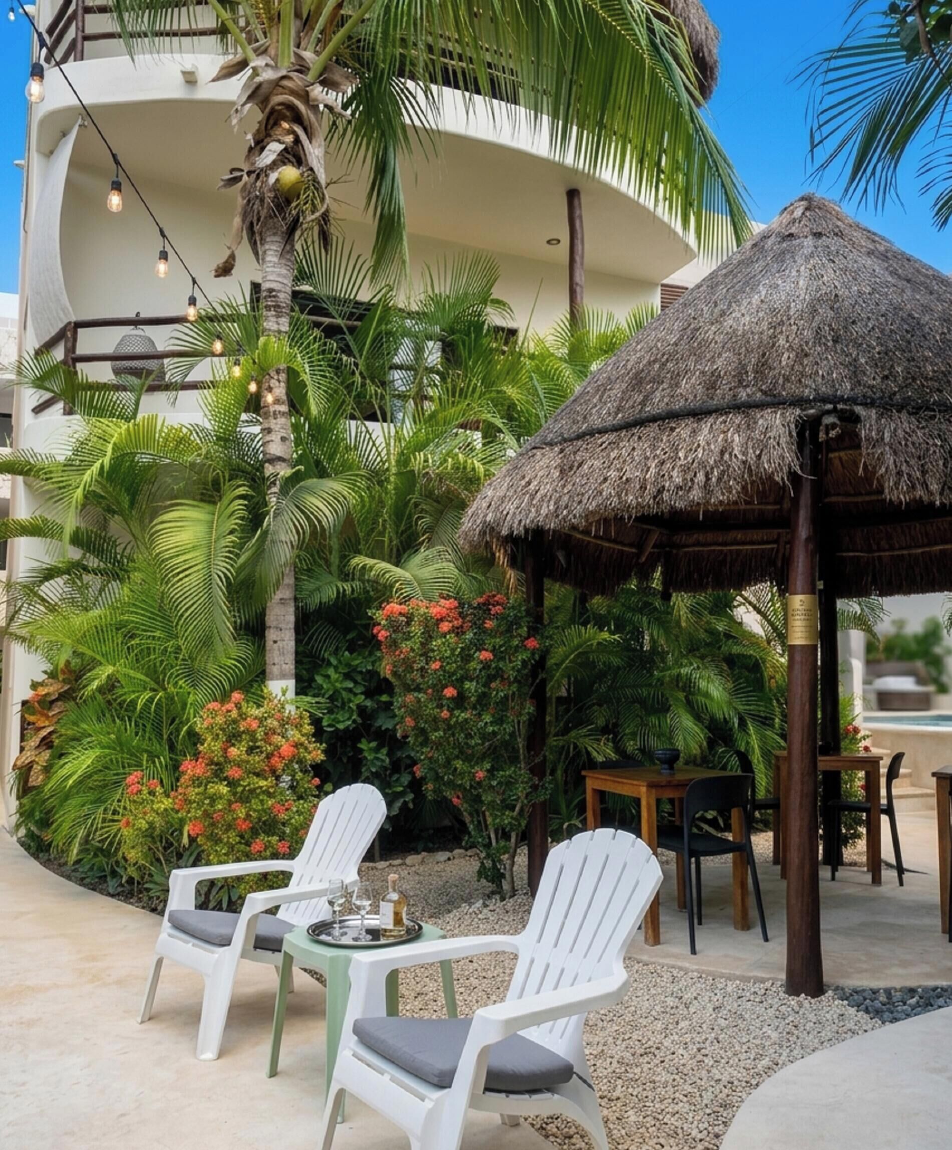 A resort patio with a thatched umbrella, white chairs, and a dining table.