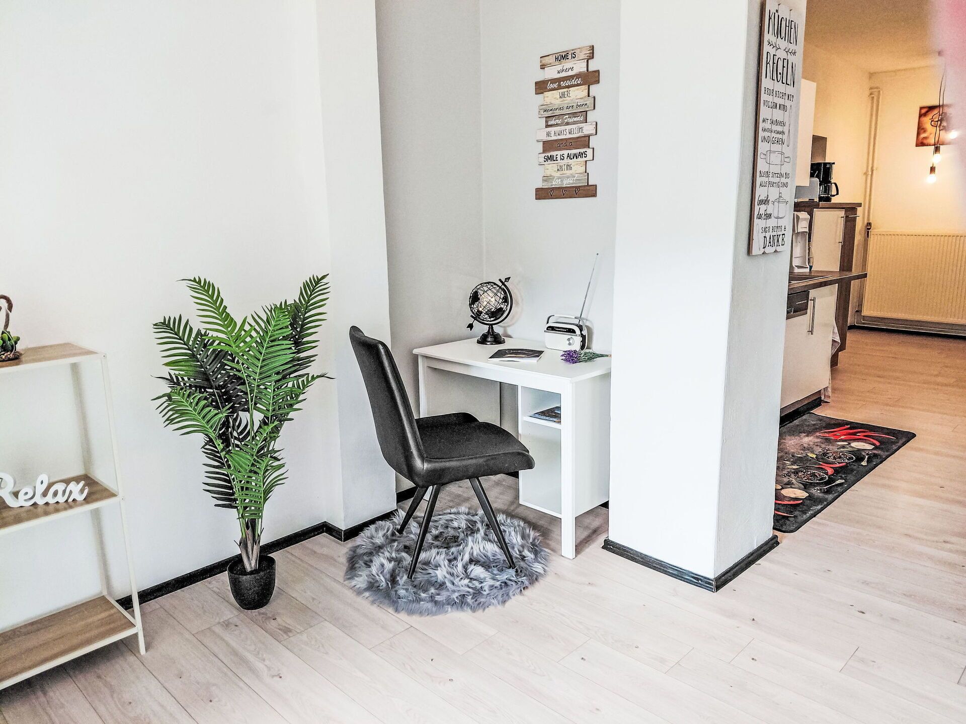 Un espace de vie compact comprenant un bureau blanc, une chaise noire, un globe terrestre et une petite plante en pot.