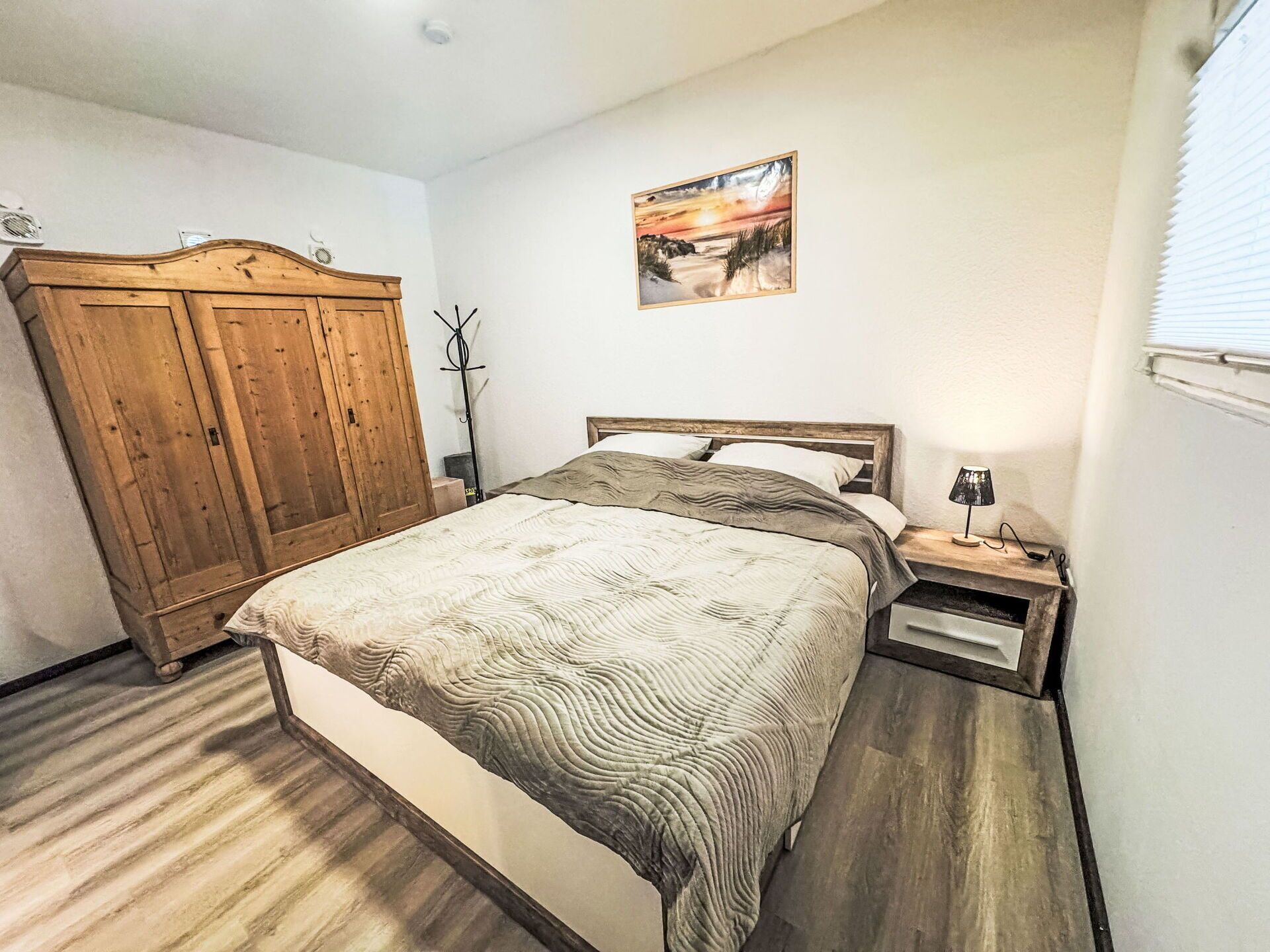 A bedroom with a wooden bed, a nightstand, a lamp, a wardrobe, and a painting on the wall.