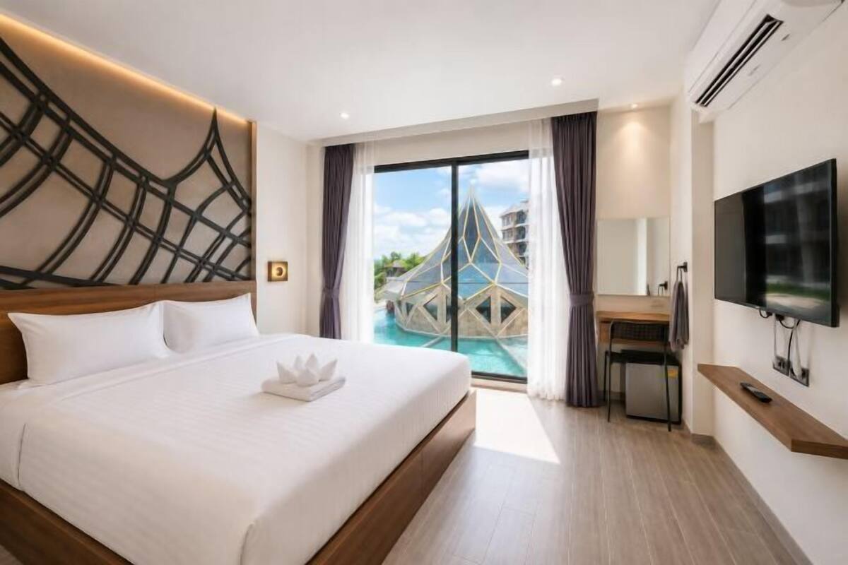A hotel room with a bed, a desk, a TV, and a view of a swimming pool.