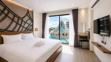 A hotel room with a bed, a desk, a TV, and a view of a swimming pool.