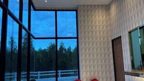 Una habitación moderna con ventanas amplias, un panel de pared con diseño geométrico y una pequeña mesa con flores rojas.