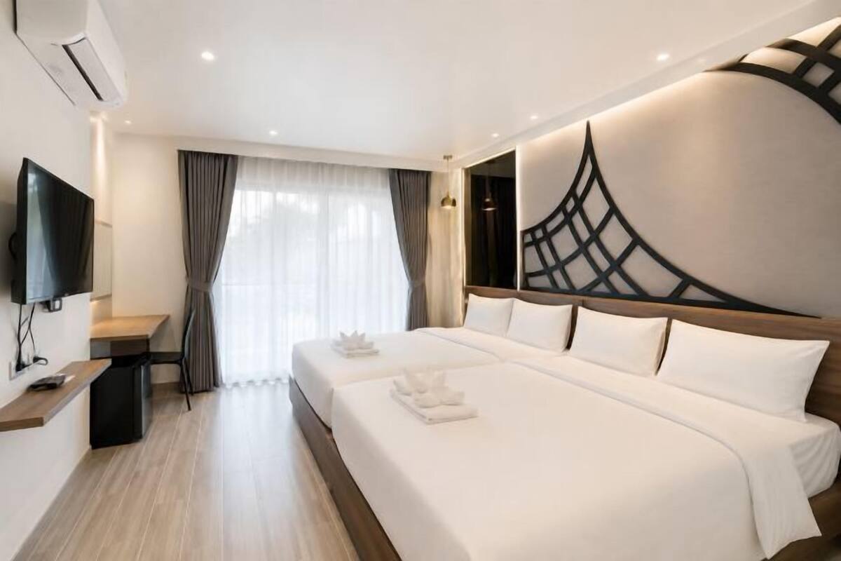 A hotel room with a large bed, a desk with a flat-screen TV, and a large window with curtains.