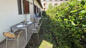 An outdoor dining area with a table set for two, chairs, and a hedge.