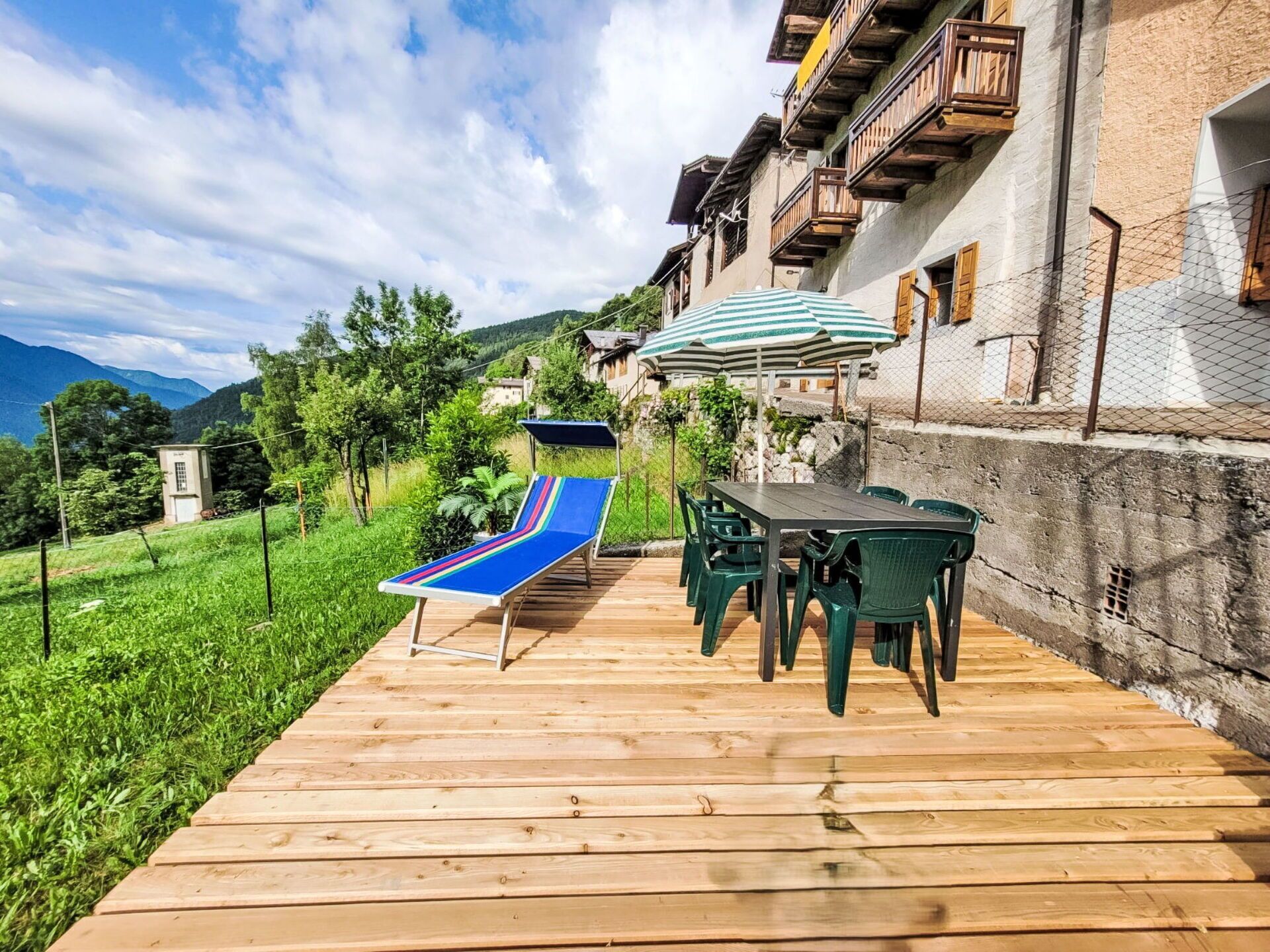 A wooden deck with a lounge chair, a table, and chairs, overlooking a mountainous landscape.