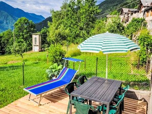 Eine Terrasse mit Tisch und Stühlen, einem gestreiften Sonnenschirm und einem blauen Liegestuhl.