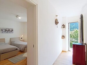 Une chambre avec deux lits, un plancher en bois, une vue sur la verdure par la porte et un radiateur rouge.
