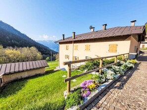 Ein traditionelles Gebäude mit einem geneigten Dach, hölzernen Geländern und einem Garten mit Blumen.