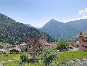 A mountainous landscape with residential buildings, a clear sky, and a tree in the foreground.
