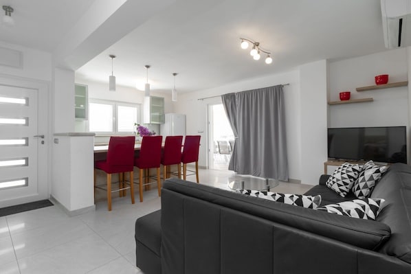 A modern living room with a black sofa, a dining area with red chairs, and a TV on a wooden stand. - Modern Villa with Pool (Blato)