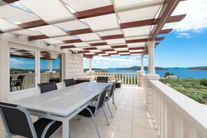 An outdoor patio with a table and chairs, a pergola, and a view of the sea. - Modern Villa with Pool (Blato)
