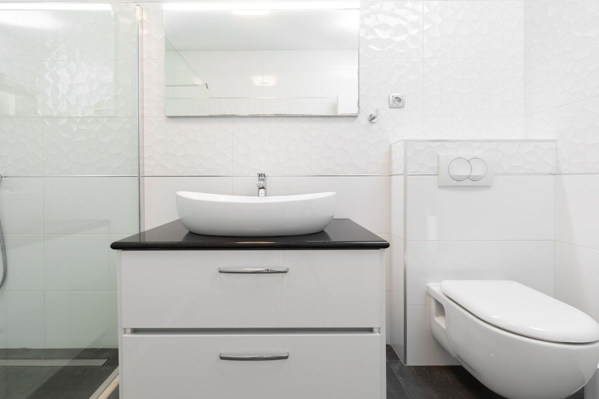 Ein modernes Badezimmer mit einem weißen Waschbecken, einer schwarzen Arbeitsplatte und einer Toilette.