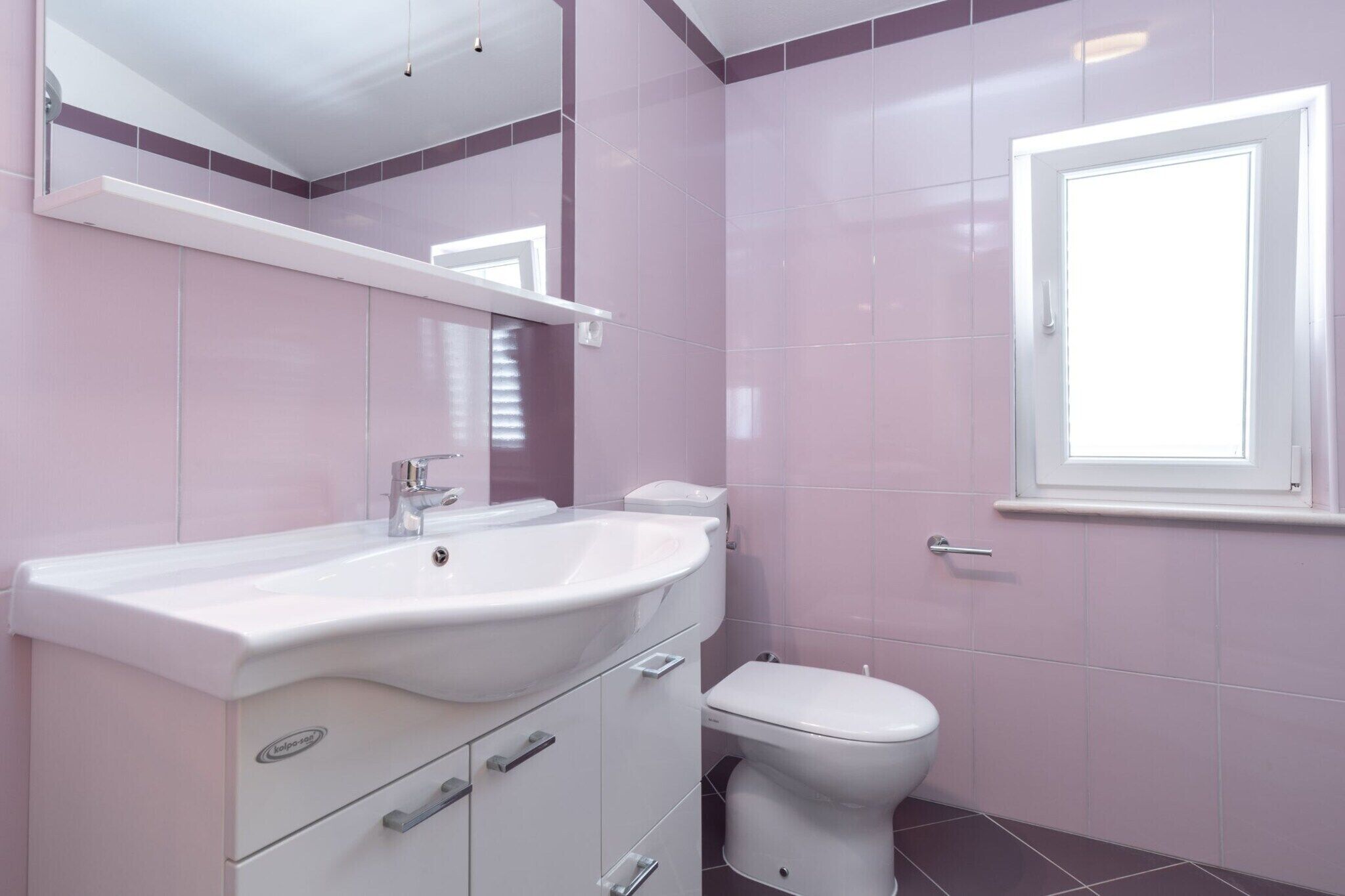 A bathroom with a white sink, a toilet, and a window.